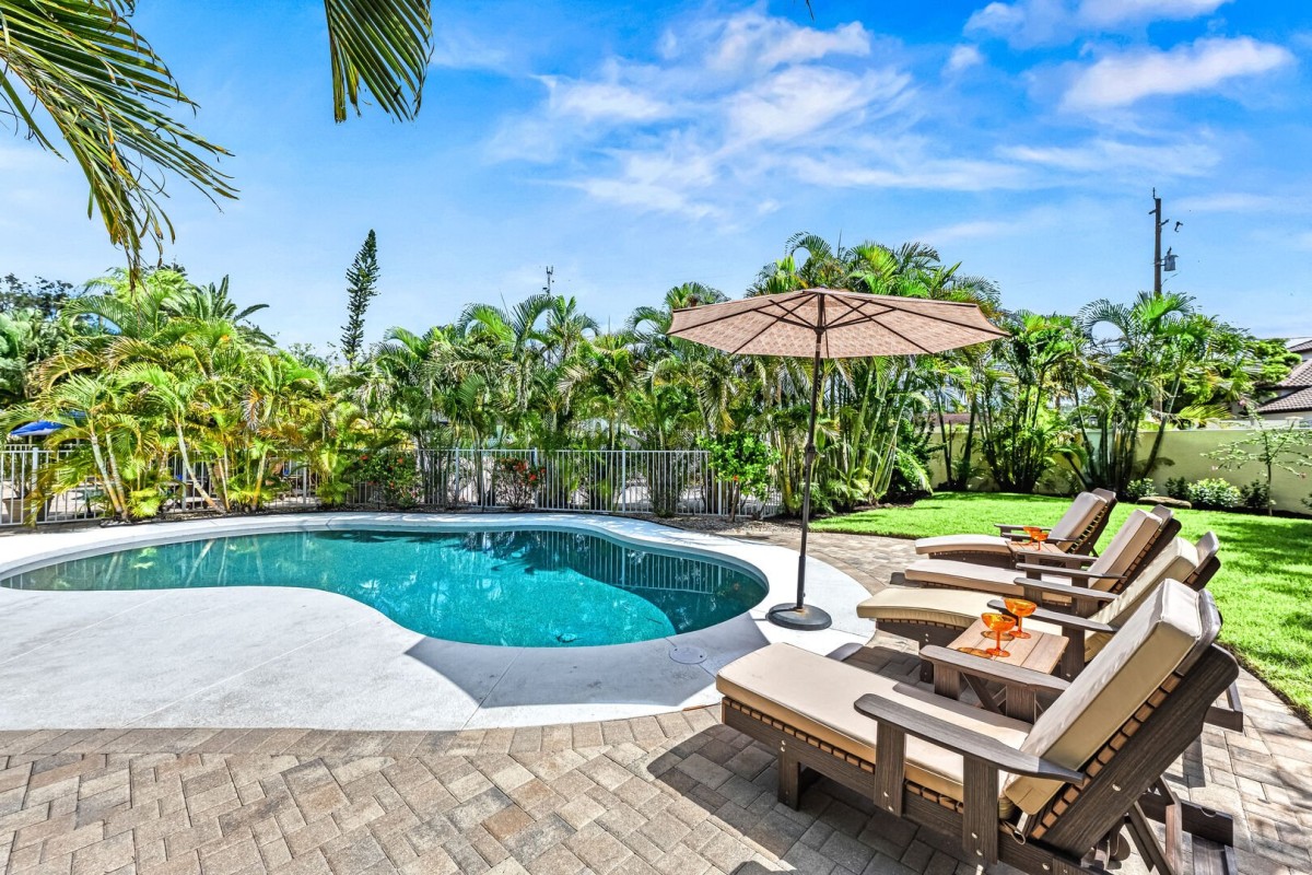 Your private heated pool sparkles invitingly under the sun, surrounded by lush palms and a quiet fence—imagine slipping into warm water anytime, the perfect refreshment just steps from your door.