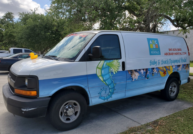White commercial transit van featuring colorful beach-themed branding graphics parked curbside.