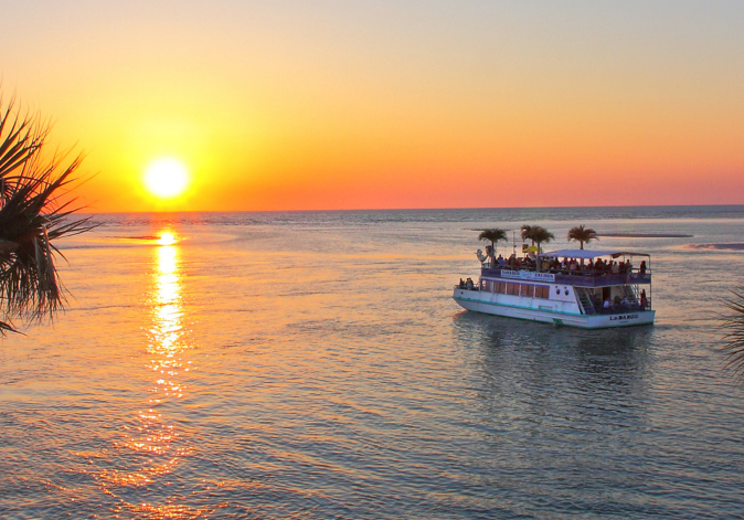 Wide ocean horizon view showing a tour boat sailing directly into a bright orange sunset.