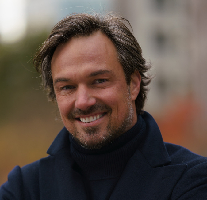 Portrait of a smiling man with brown hair wearing a dark sweater.