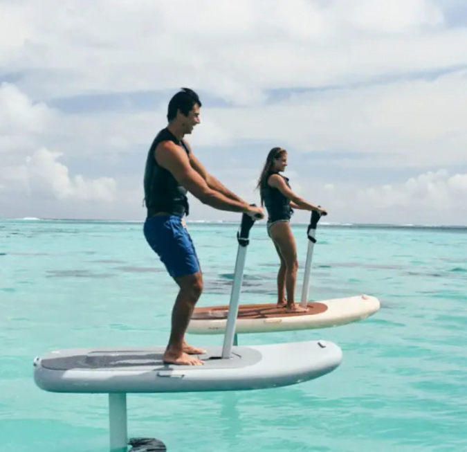 Two people paddleboarding across bright blue tropical water on a clear sunny day.