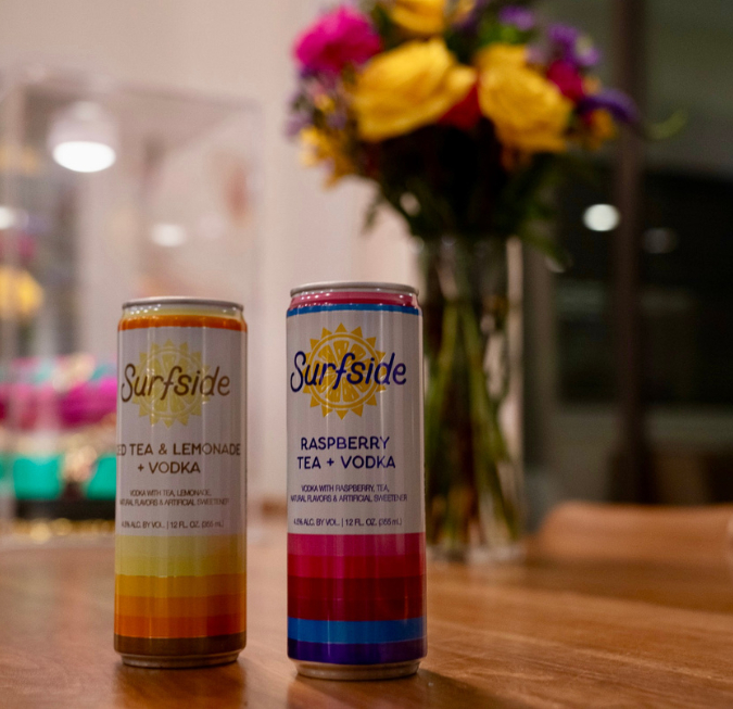 Two slim aluminum energy drink cans sitting on a bar next to a flower vase.