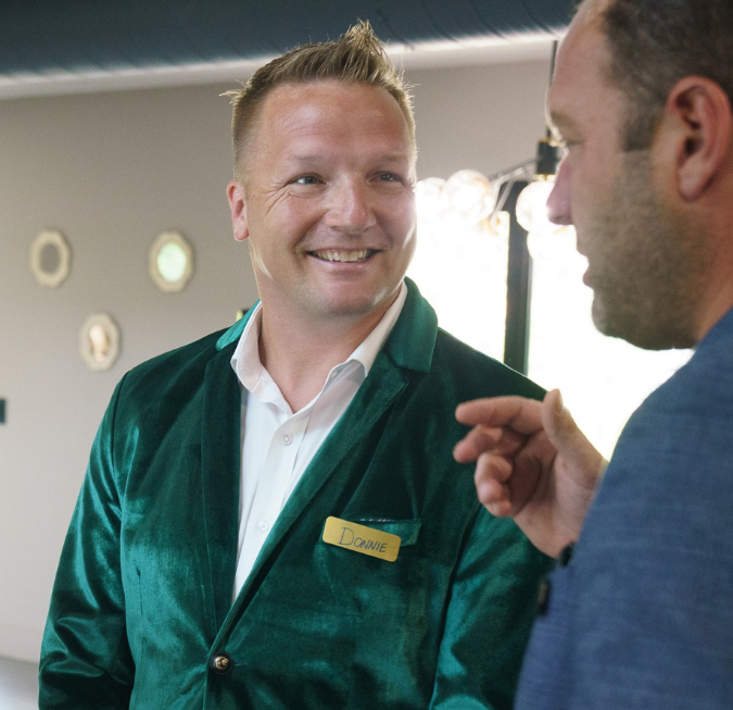 Smiling professional man wearing a green velvet blazer chatting with someone.
