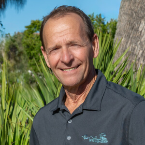 Portrait of a smiling male employee with short hair in front of palm trees.