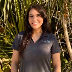 Smiling female team member with long brown hair wearing a dark polo shirt.