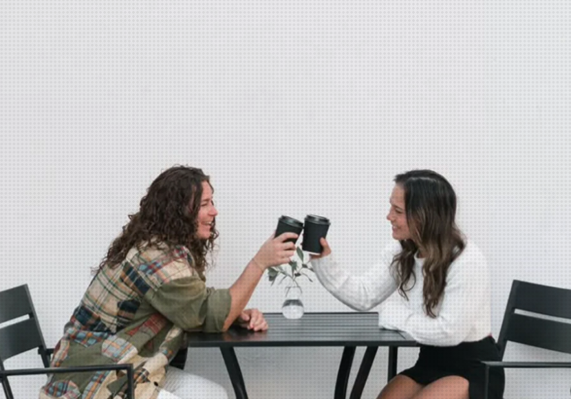 Two women clinking glasses together while seated at an outdoor restaurant.