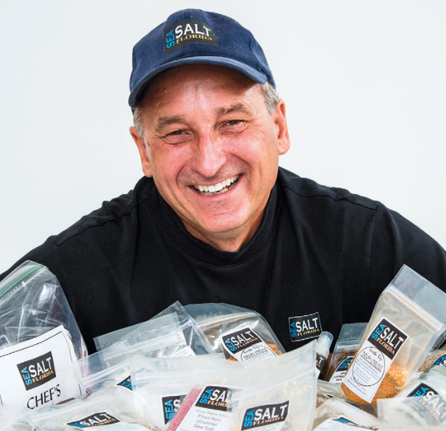 Smiling private chef wearing a black uniform and baseball cap.