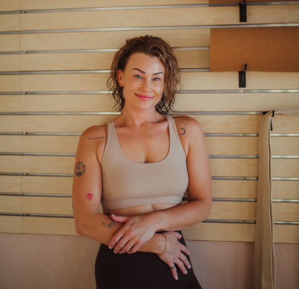 Smiling woman in athletic wear posing inside a yoga or fitness studio.