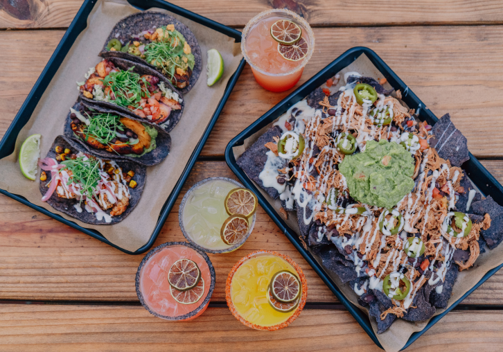 Overhead view of fresh tacos and vibrant specialty cocktails served on a tray.